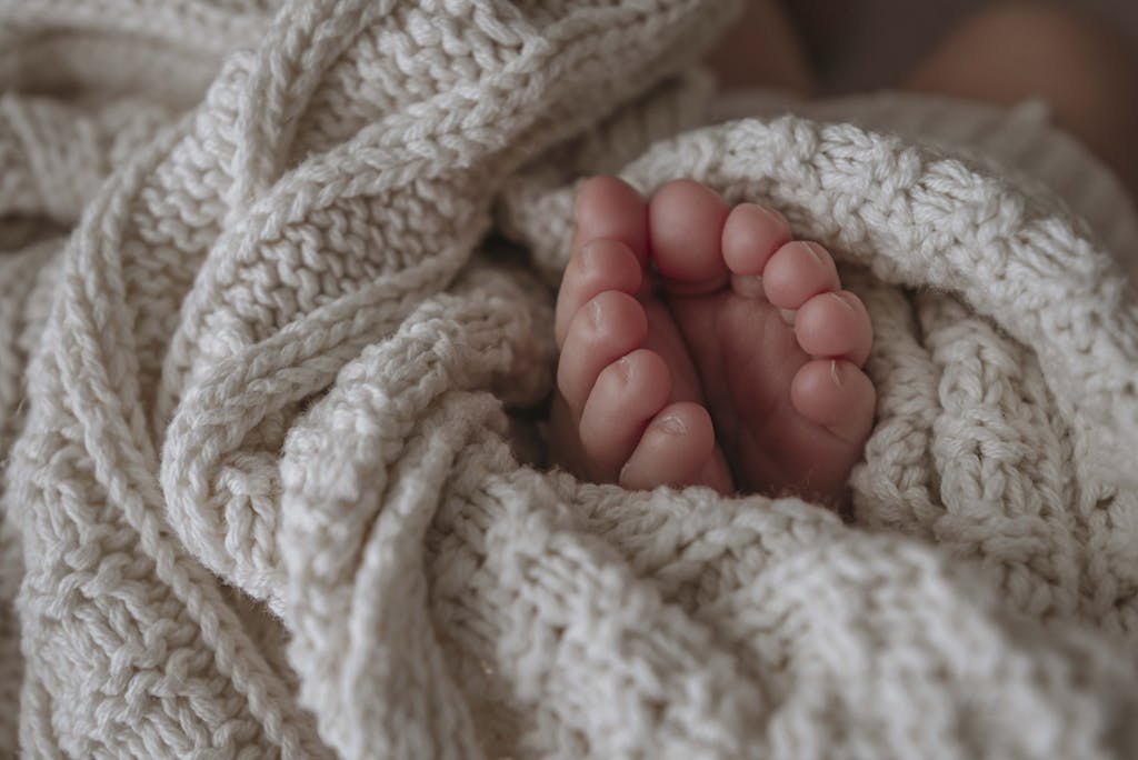 Adorable baby feet peeking out from a warm knitted blanket, capturing warmth and comfort.