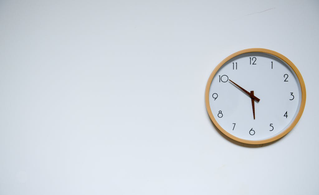 Simple wall clock with wooden frame against a white background, showing the time 10:10.