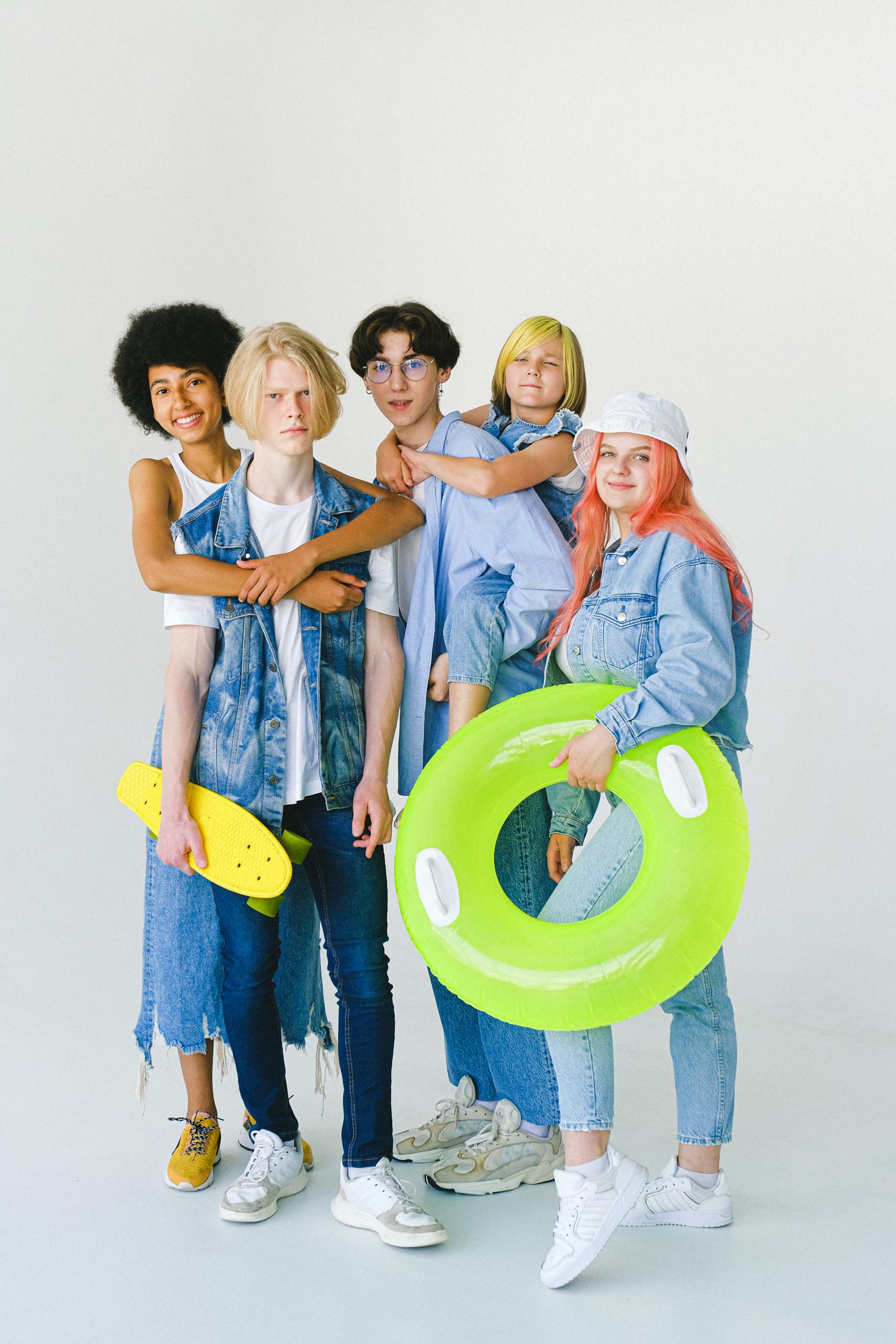 A diverse group of teenagers posing in studio with skateboards and inflatable ring, radiating youthful energy.