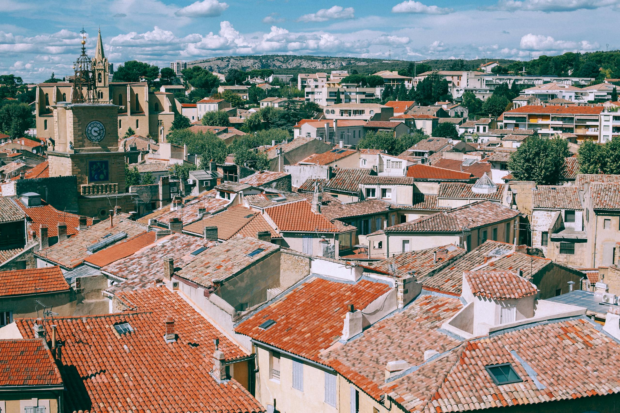 Cityscape of old town with classic dwell houses with red tiled shabby roofs and vegetation under blue sky with clouds
