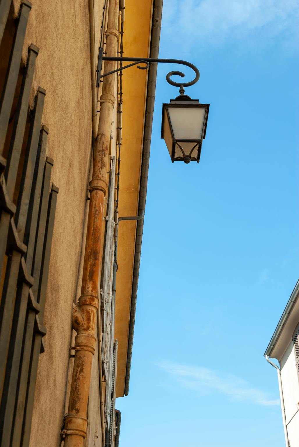 Vintage street lamp on a historic facade in Aix-en-Provence against a clear blue sky.