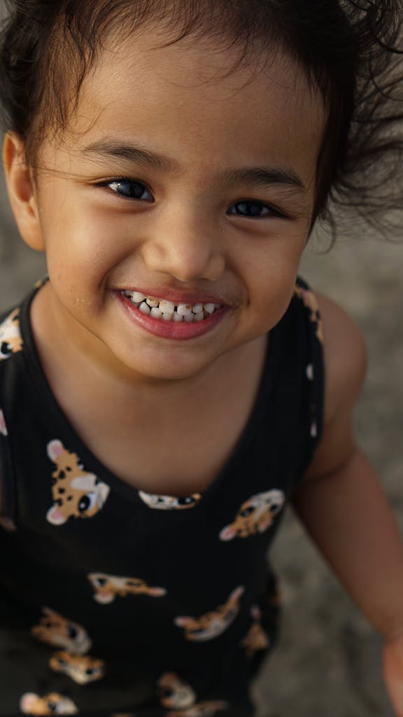 A joyful South Asian toddler smiling wearing a leopard print dress outdoors in India.