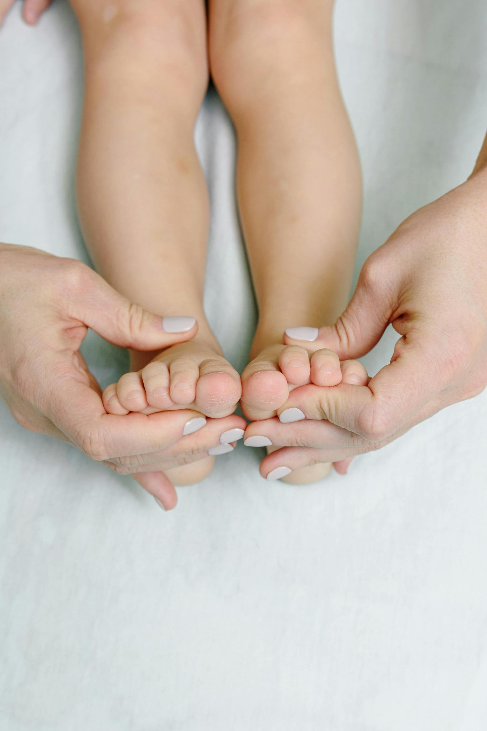 Close-up of hands giving a calming foot massage to a baby's feet on a soft surface.