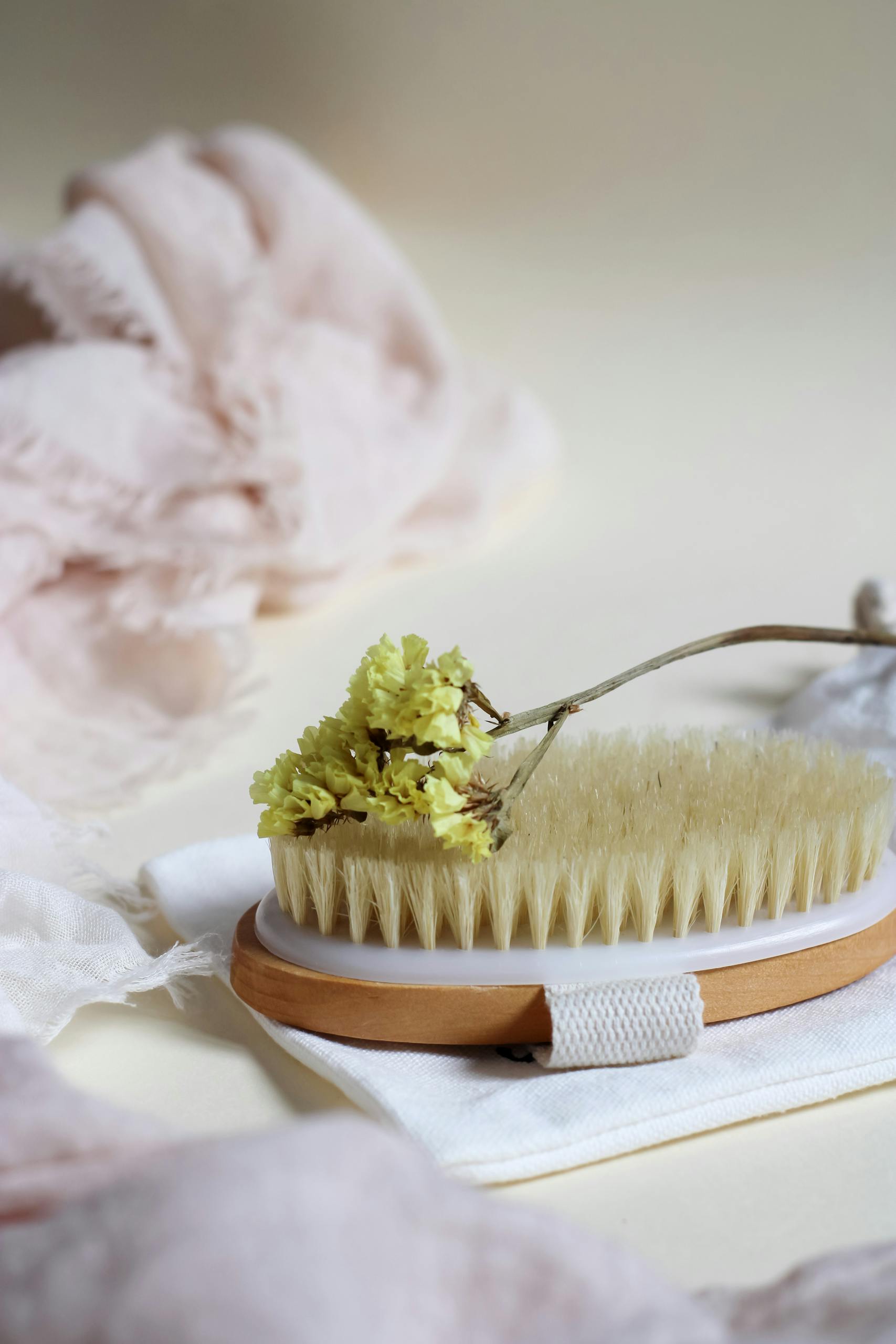 Wooden body scrub brush with dried flower on soft textiles creates a spa-like atmosphere.